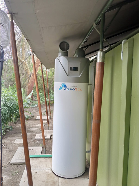 a white water heater heat pump sitting in the shade under a tent